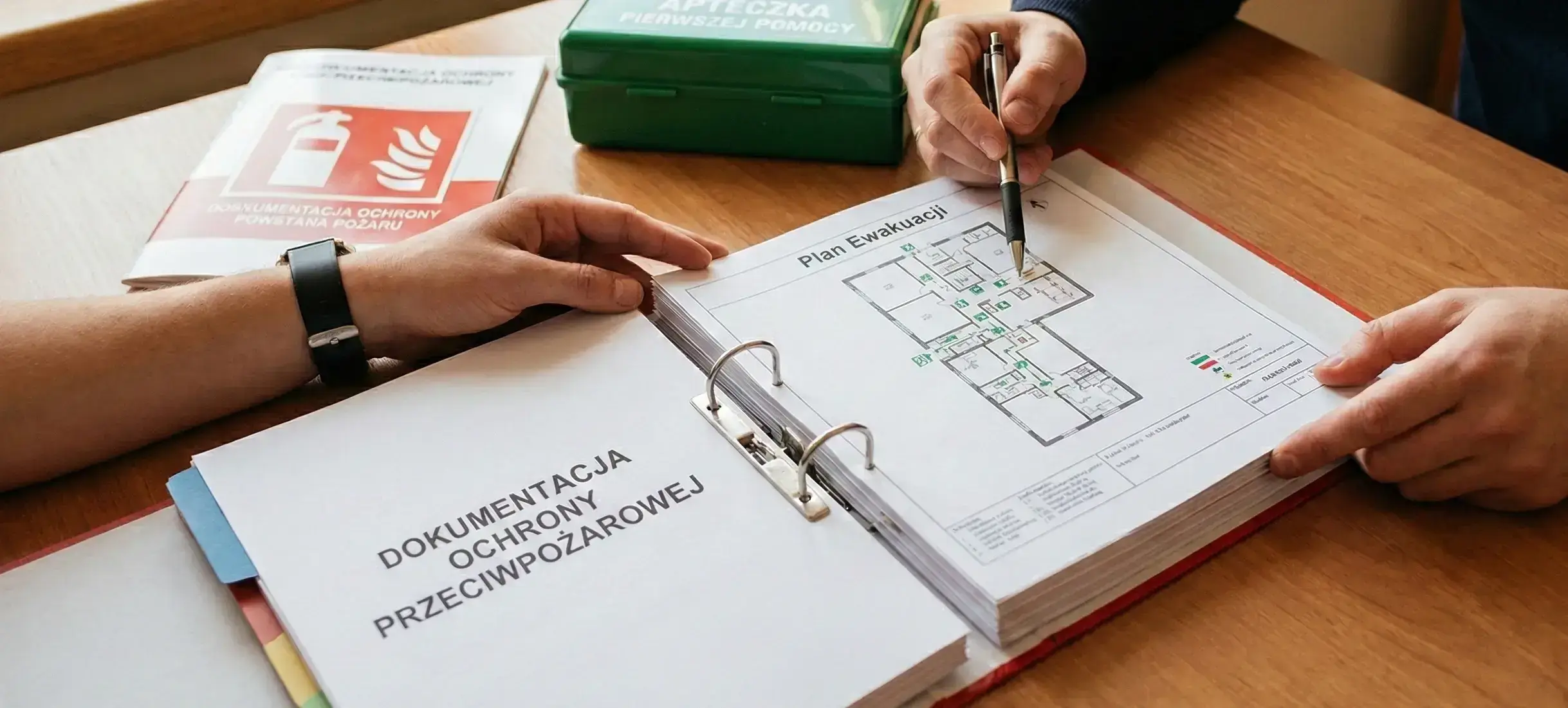Konsultacja w zakresie ochrony przeciwpożarowej: specjaliści omawiający plan ewakuacji w otwartej dokumentacji ochrony przeciwpożarowej.