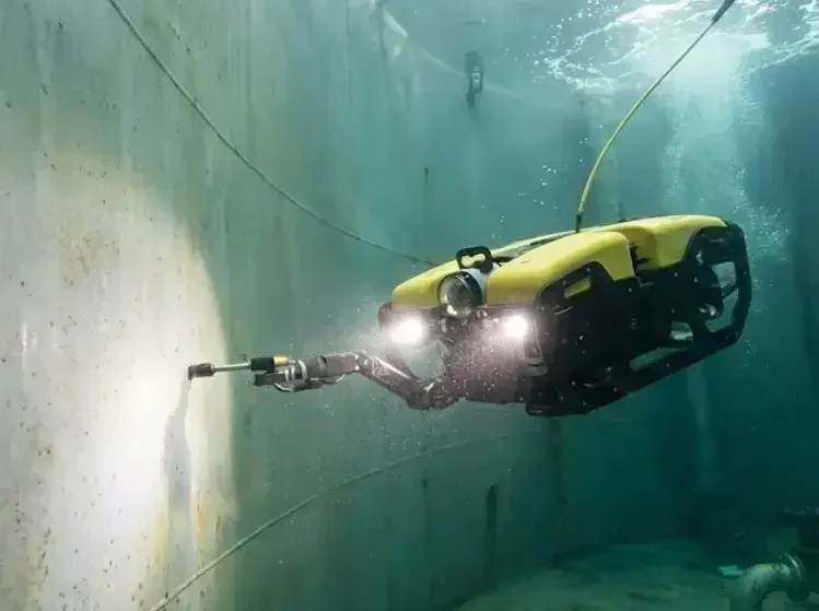 Żółty dron podwodny (ROV) oświetlający reflektorami ścianę zbiornika podczas inspekcji technicznej pod wodą.